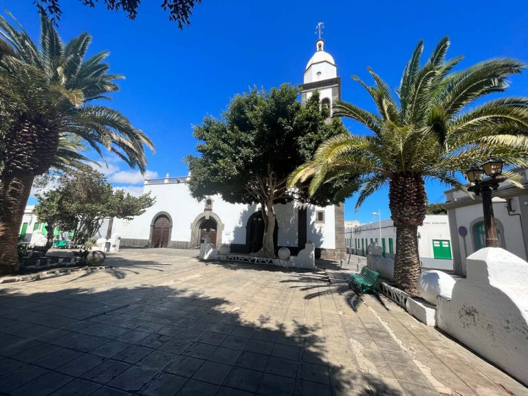 small colonial squate with palm trees and a whitewashed church with bell tower