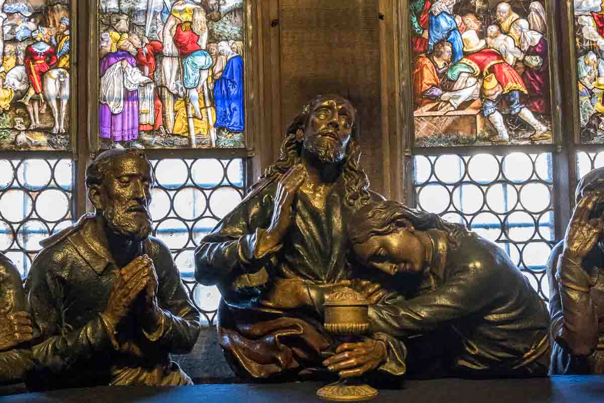 carving of jesus and 2 disciples at the last supper behind stained glass windows