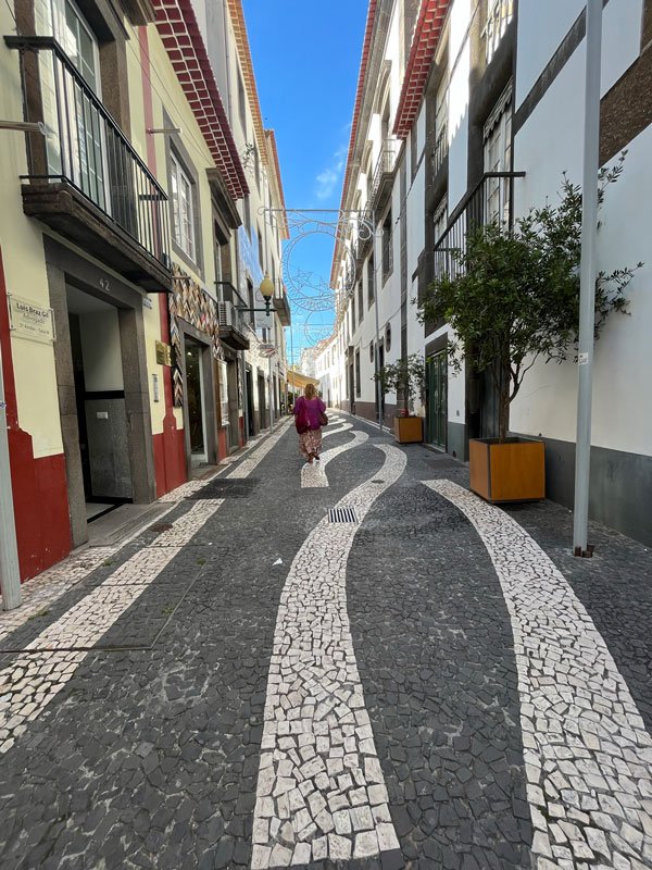 woman walking along a narrow street paved with black and white mosaics in funchal