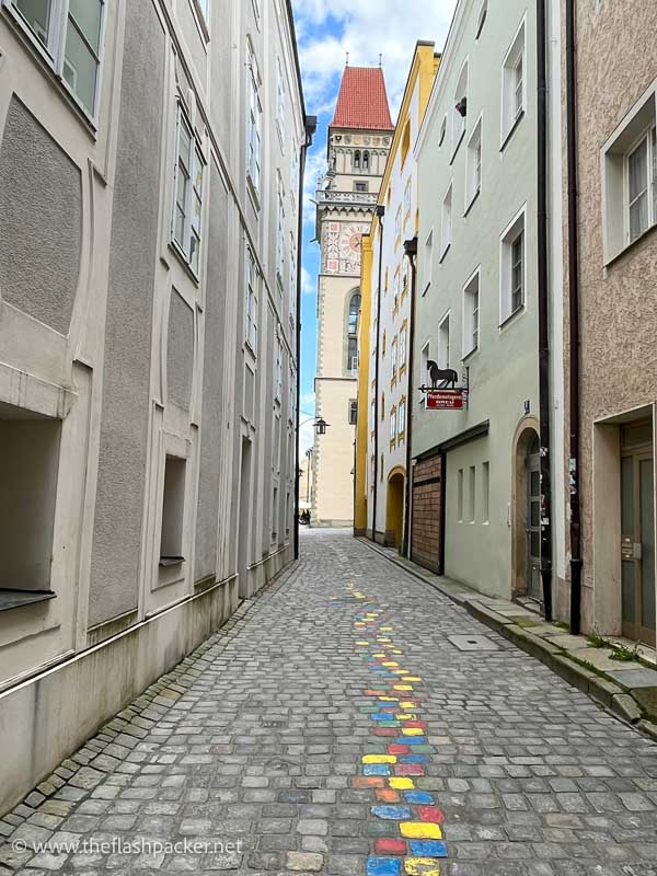 cobbled street in passau with squares of rainbow coloured paint in the middle and a clock tower at the end