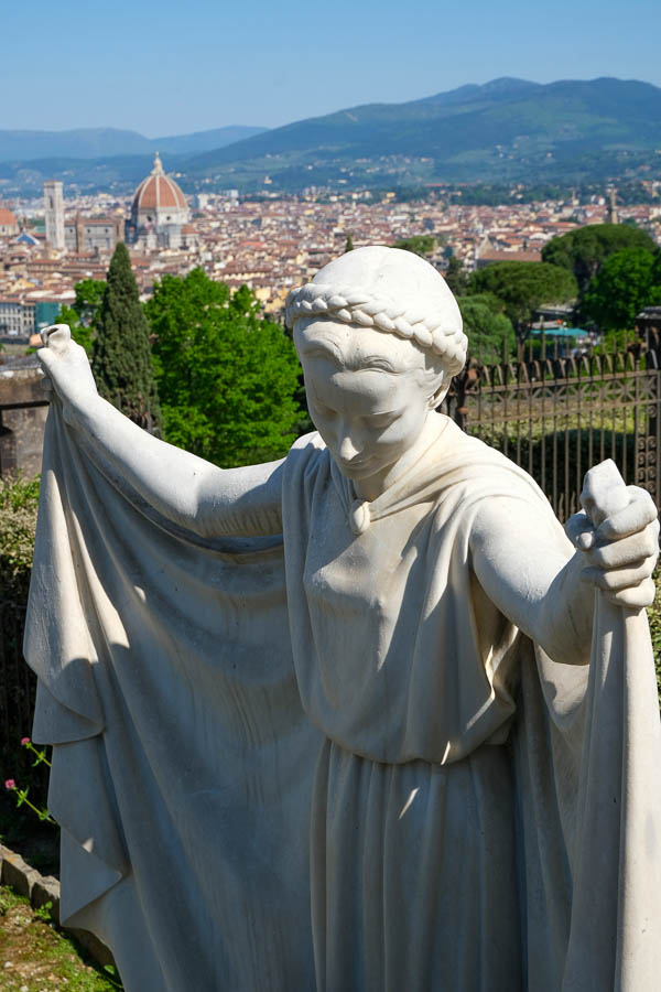 statue of angel with arms outstretched in front of the skyline of florence italy