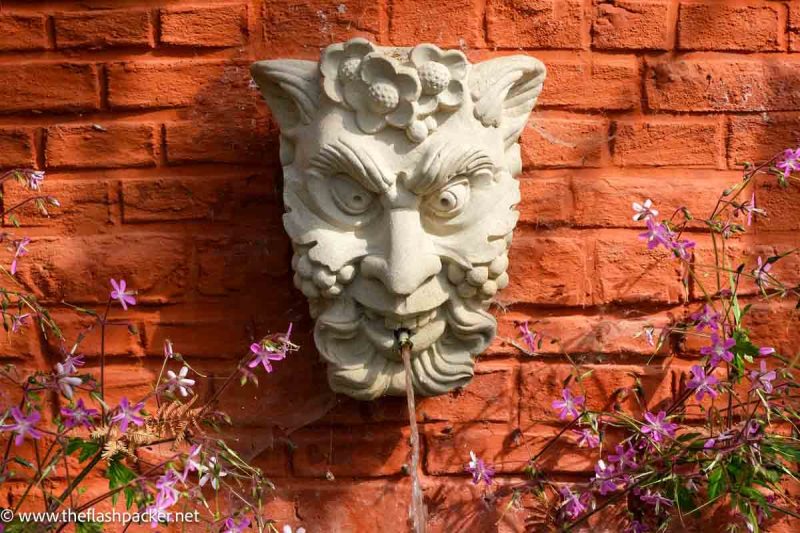 Visiting De Kruidtuin Leuven: Belgium's Oldest Botanical Garden 1 stone fountain of face of satyr against a terracotta wall at leuven botanical garden