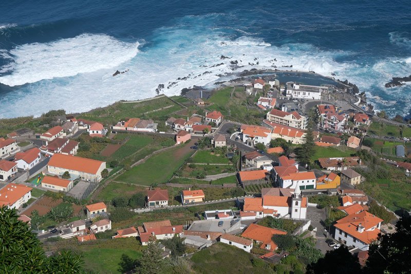 red roofs of small village of porto moniz in madeira next to crashing waves of ocean