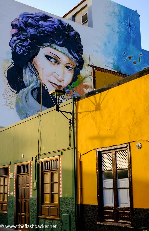 weathered ochre coloured buildings with wooden doors  and mural of womans face