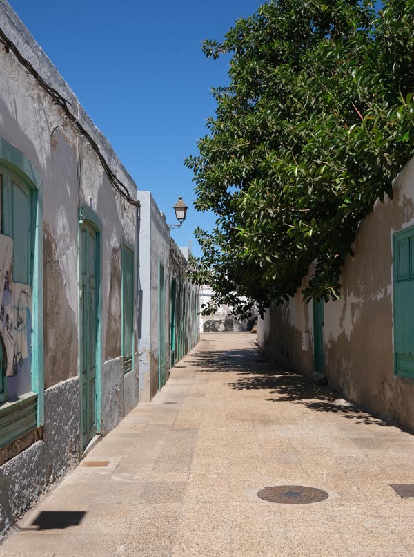 narrow street lined with single storey buildings with green doors