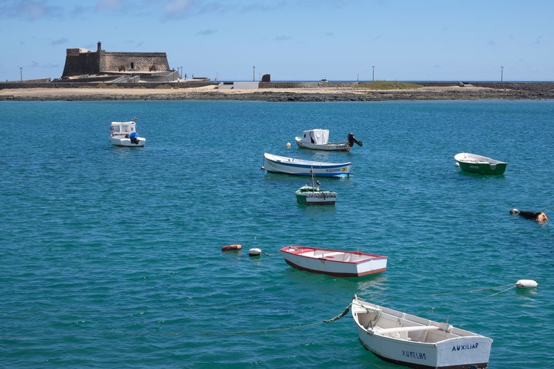 small boats in a harbour in front of a small stone fortress in arrecife in lanzarote