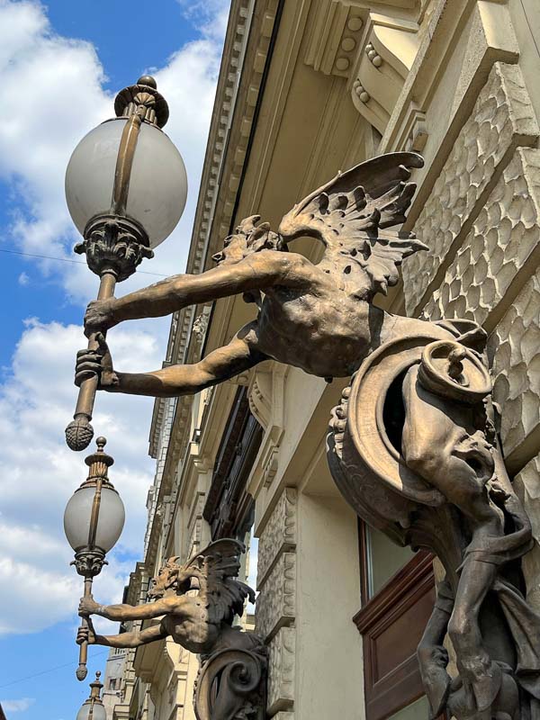mythological creature with wings holding a lamp on the exterior of budapest new york cafe