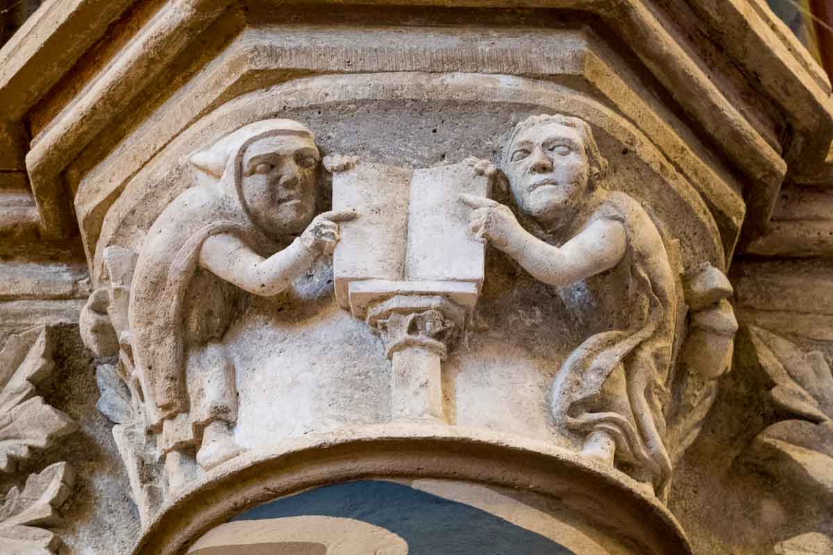 stone carving of 2 figures pointing to a book