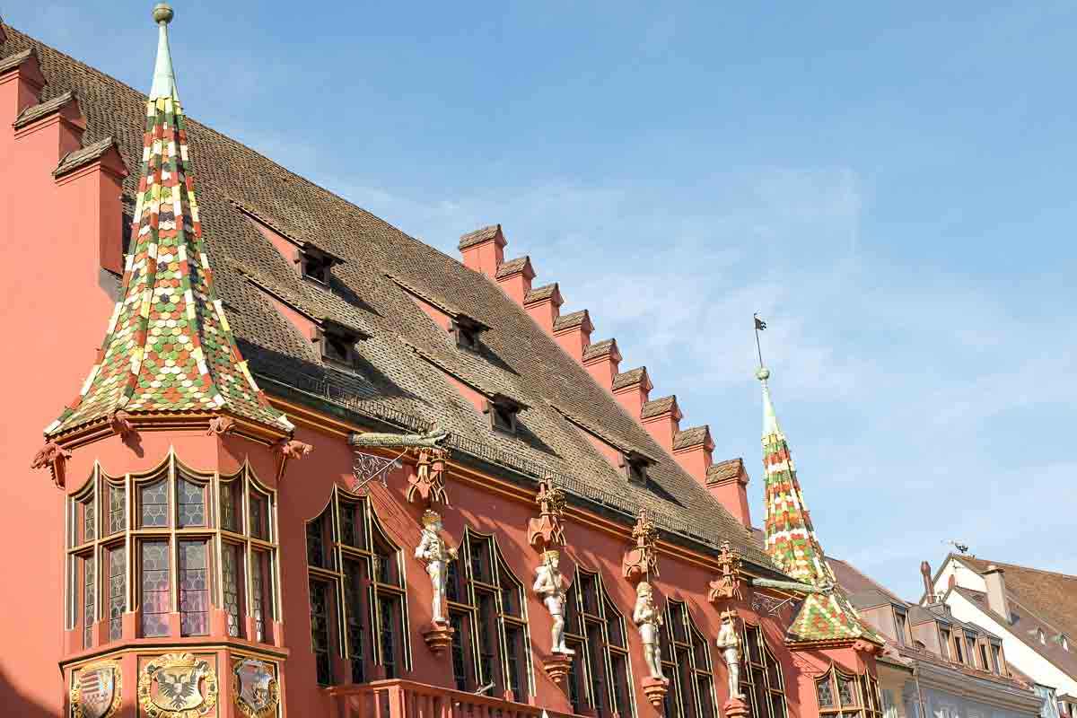 multicoloured tiled spires and external sculptures on front of a medieval salmon coloured building