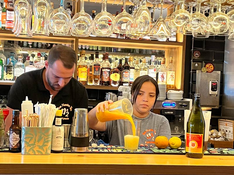 woman behind a bar making poncha pouring a citrus drink into a glass from a jug