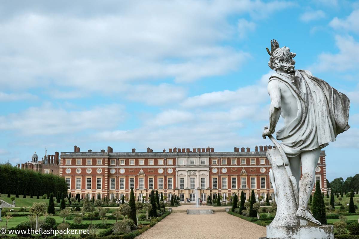 Large statue overlooking wide red brick exterior of hampton court palace
