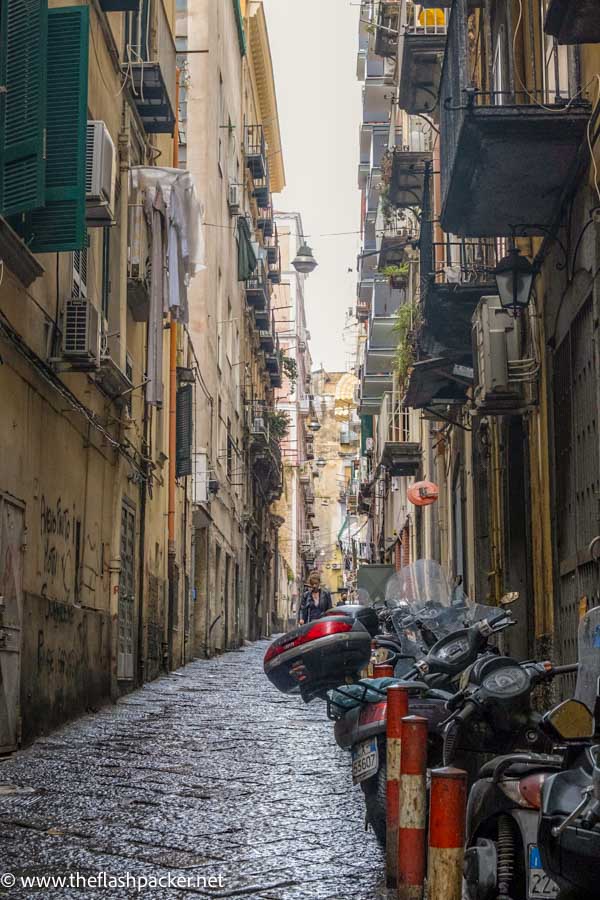 person walking down narrow street with row of scooters