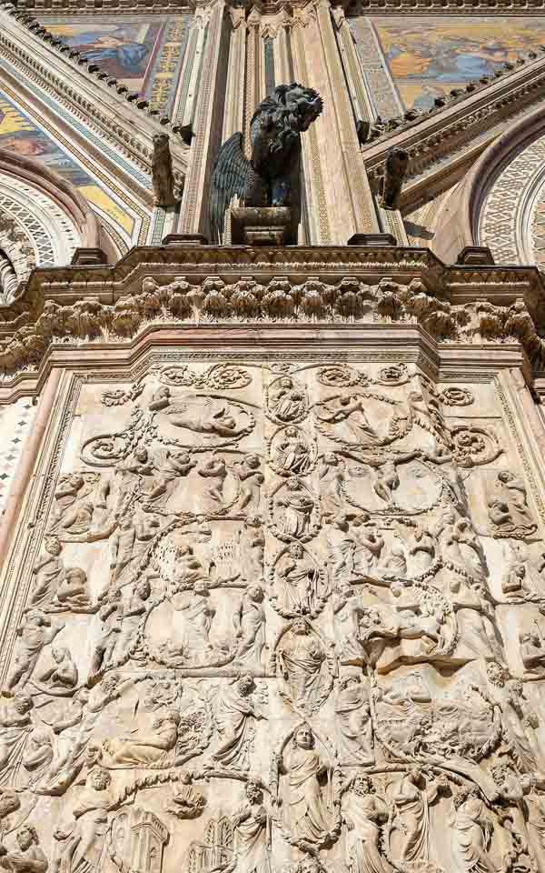 finely carved stone tracery on outside column of orvieto cathedral topped by bronze sculpture of lion