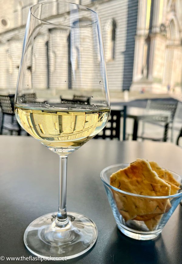 a glass of red wine and a small bowl of crackers on a table outside Orvieto cathedral