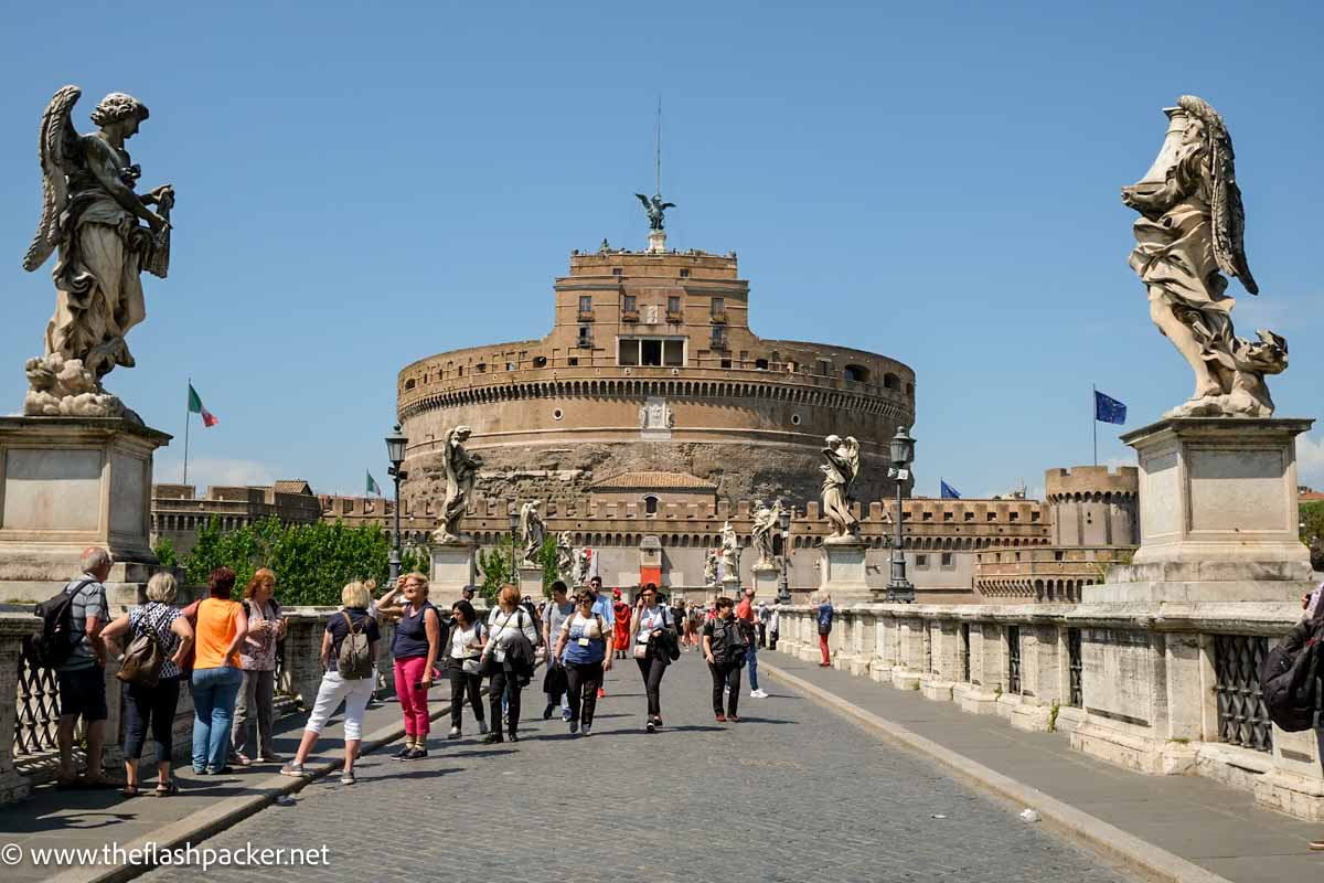 8 Awesome Angels and Demons Locations in Rome (+ Map) 1 people walking across bridge to the large circular fort in rome of castel sant-angelo