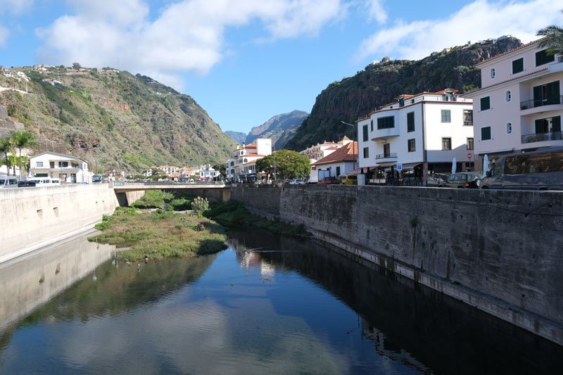 small town with white buildings on the banks of a river bed with reflections in water