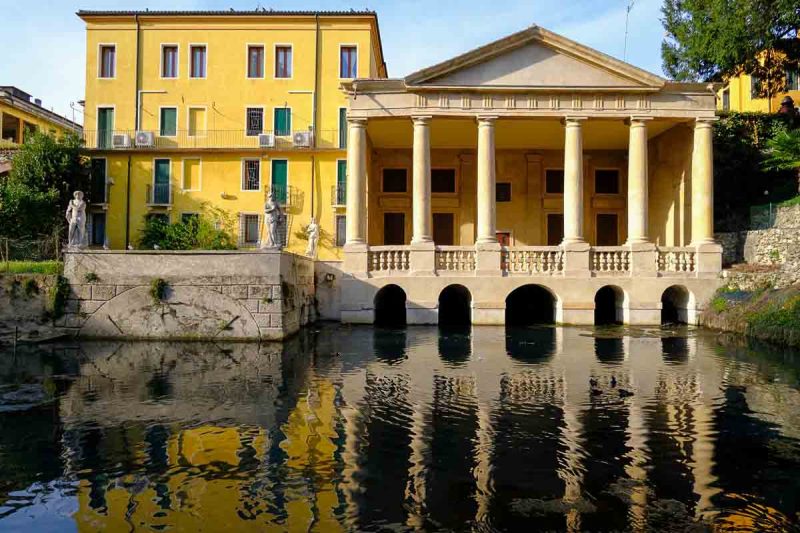classical villa with portico and yellow building reflected in pond in vicenza salvi gardens