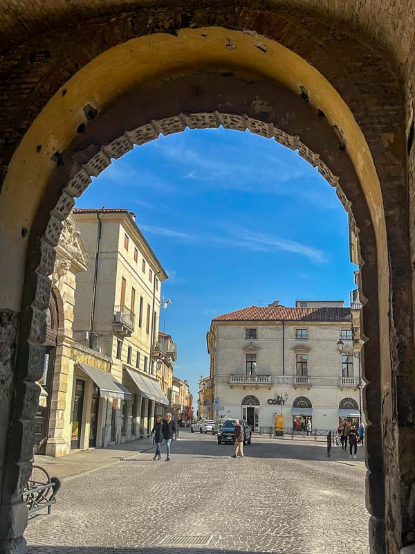 people walking in cobbled street in vicenza historic centre viewed through an arch
